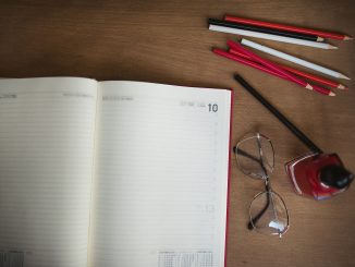 Cuaderno abierto y lápices de colores sobre un escritorio de madera